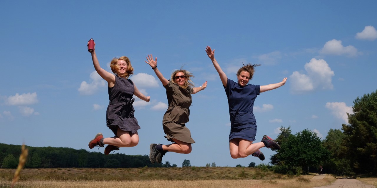 drie vrouwen springen in de lucht in hun wandeljurkjes.