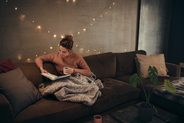afbeelding van een vrouw die op de bank een boek leest.