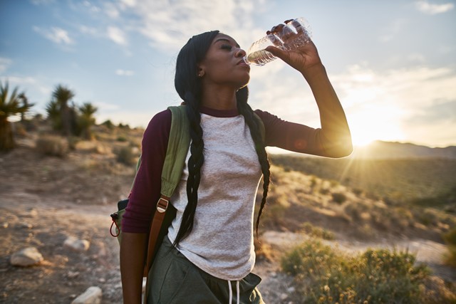 vrouw drinkt water uit een flesje in de zon.