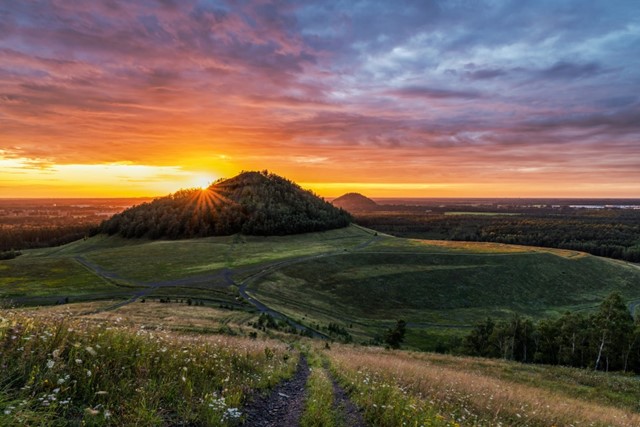 foto van een zonsondergang in een heuvelachtig, groen landschap.