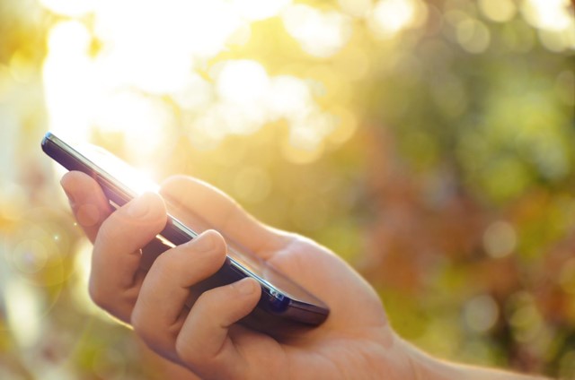 afbeelding van iemand die buiten zijn mobiele telefoon in de hand heeft.