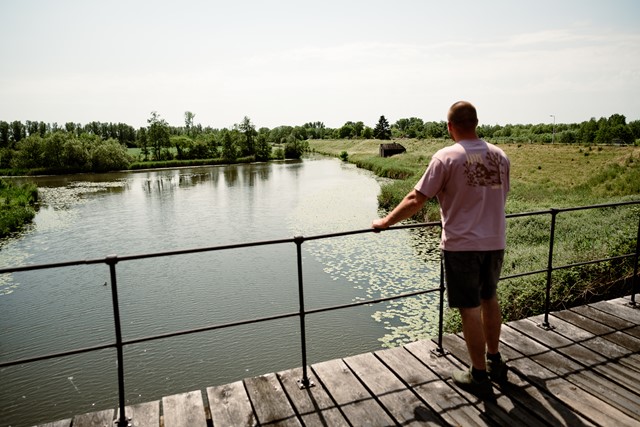 Man kijkt vanaf een bruggetje het water en polderlandschap over