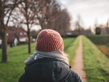 Vrouw met muts van achterkant op een wandelpad