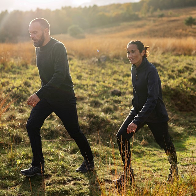 man en vrouw wandelen op heuvelachtig graslandschap.