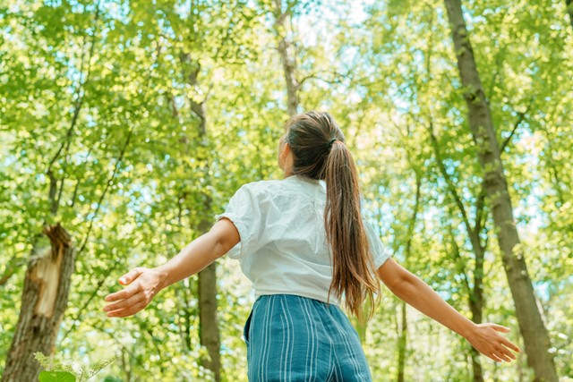 vrouw kijkt omhoog naar de zon in het bos.