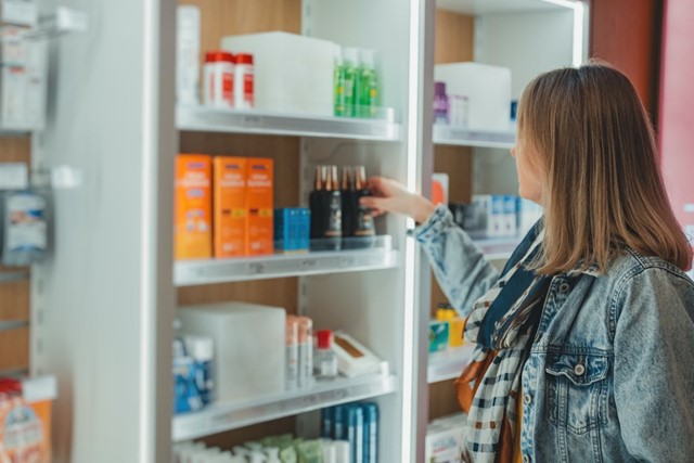 Zomerse wandeling? Smeren, smeren, smeren!; vrouw pakt zonnebrand uit een winkelschap