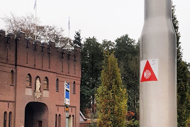 afbeelding van de Abdij Onze Lieve Vrouw van Koningshoeven met een sticker van de Camino op een lantaarnpaal.
