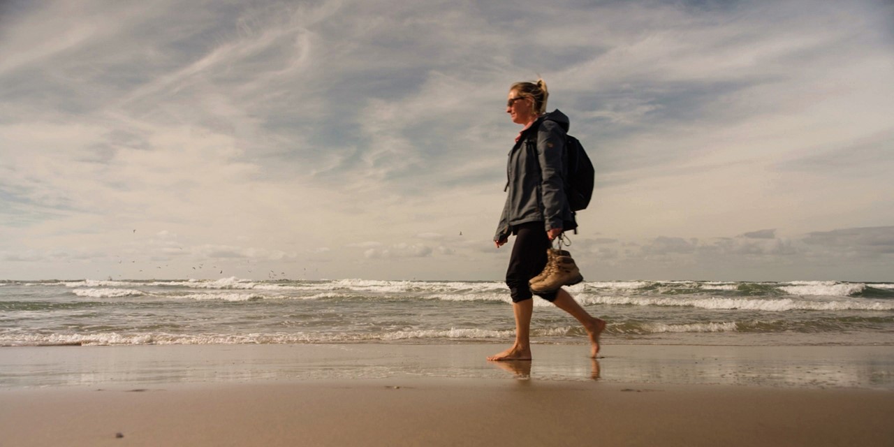 afbeelding van een vrouw die op blote voeten wandelt op het Texelse strand.