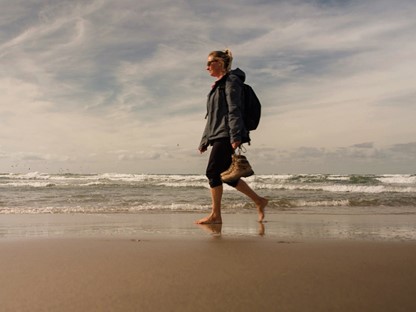afbeelding van een vrouw die op blote voeten wandelt op het Texelse strand.