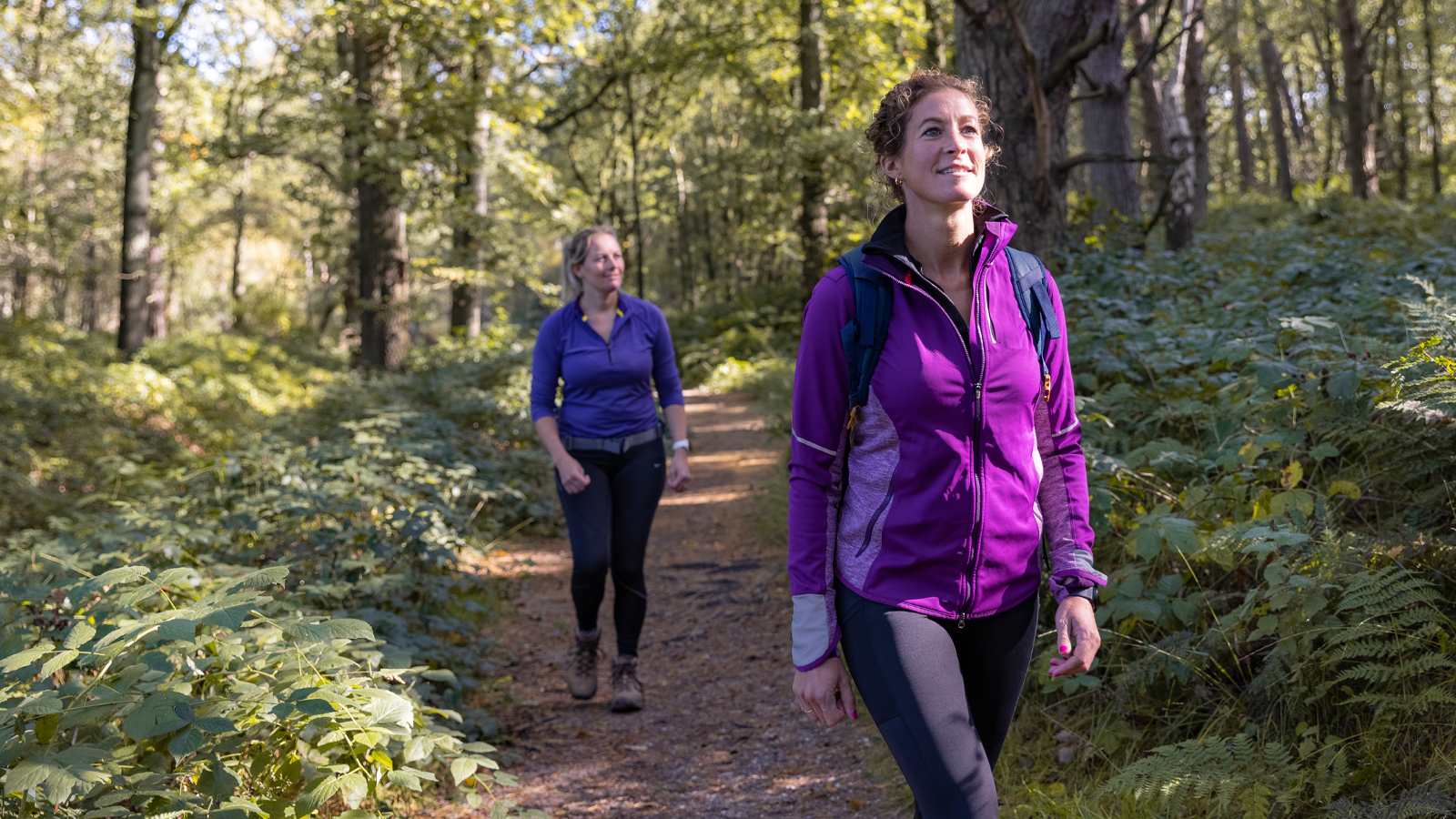 Twee sportief geklede vrouwen wandelen door het bos