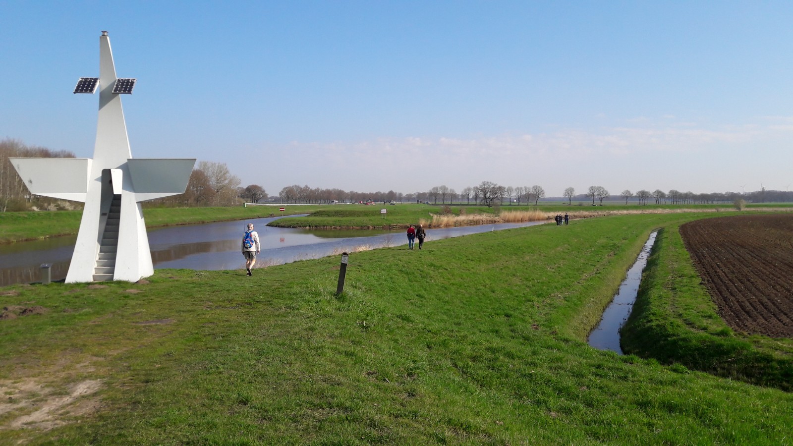afbeelding van wandelaars in een groen landschap met een wit kunstwerk.