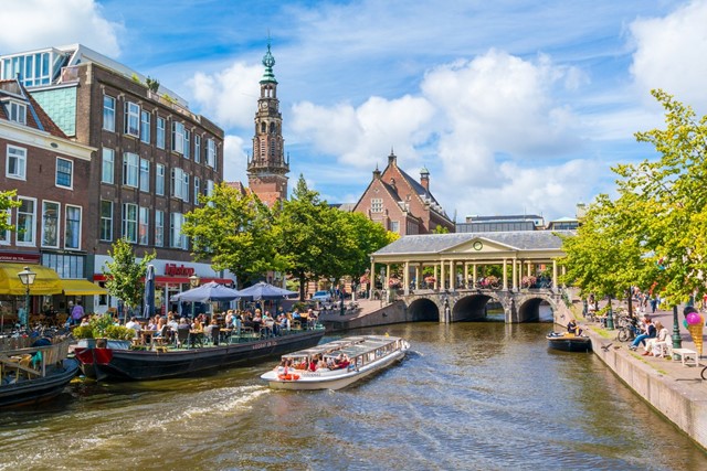 afbeelding van een Leidse gracht met een rondvaartboot en terrasjes.