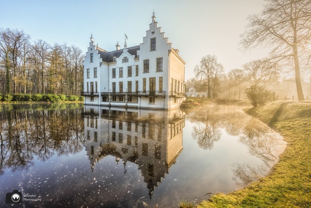 kasteel in het zonlicht met spiegeling in het water.