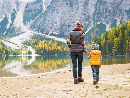 Vrouw en zoon wandelen op zand met uitzicht op het water en de bergen