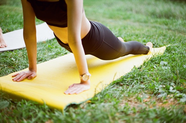 vrouw doet yoga op geel matje op het gras.