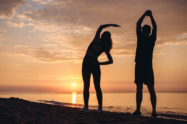 Man en vrouw stretchen tijdens zonsopkomst op het strand