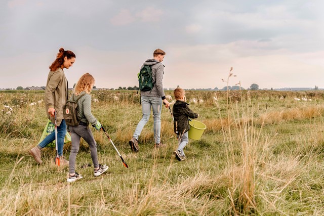 vader, moeder en twee kinderen wandelen over het gras met een afvalgrijper en vuilnisemmer.