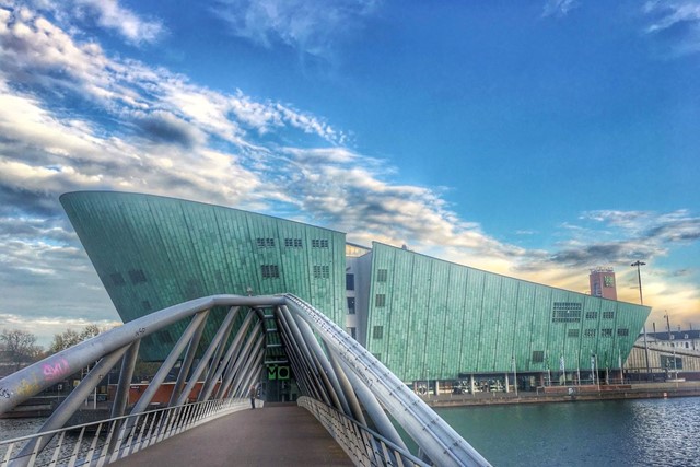 afbeelding van het NEMO Science Museum, een futuristisch groen gebouw achter een brug.
