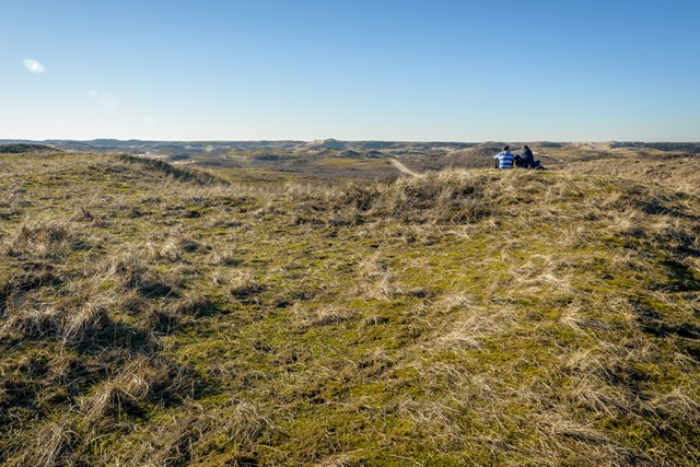 Twee wandelaars zitten in de duinen van Zandvoort.