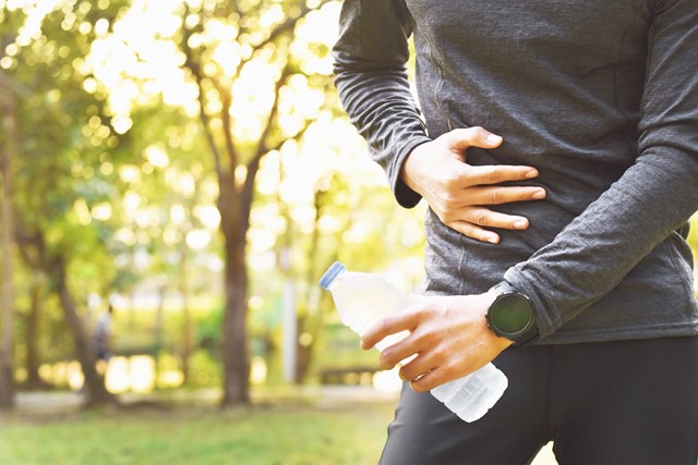 man grijpt naar buik met flesje water in zijn hand.