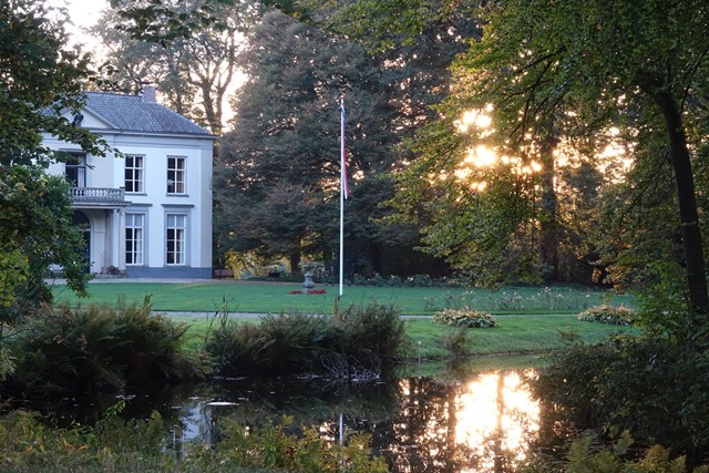 afbeelding van een landhuis in de Colckhof, met een ondergaande zon, weerspiegeld in het water.