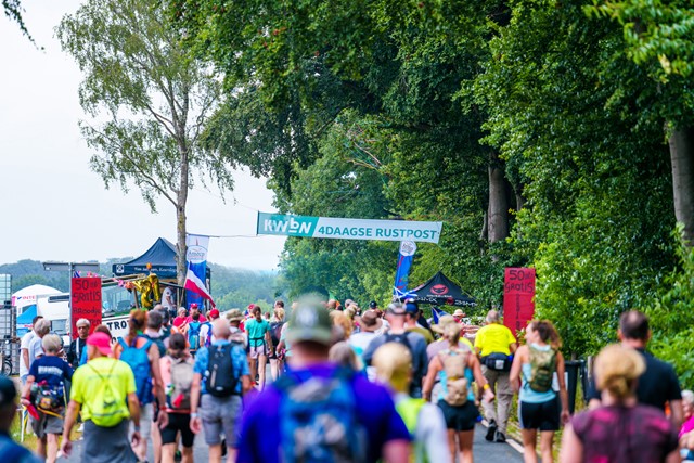 wandelaars tijdens de 4Daagse Nijmegen en een vlag van de KWbN 4Daagse Rustpost.