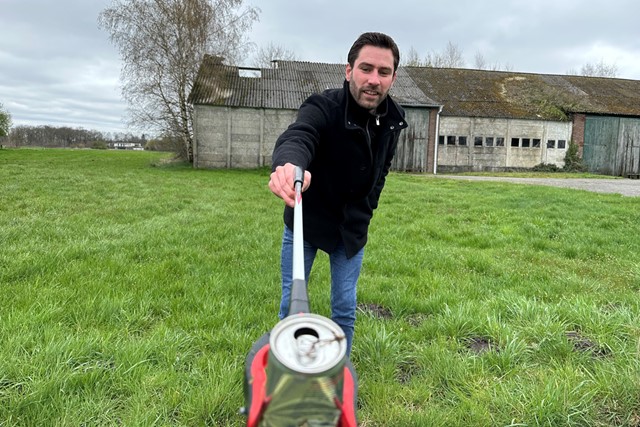 man met afvalgrijpstok en blikje op het gras