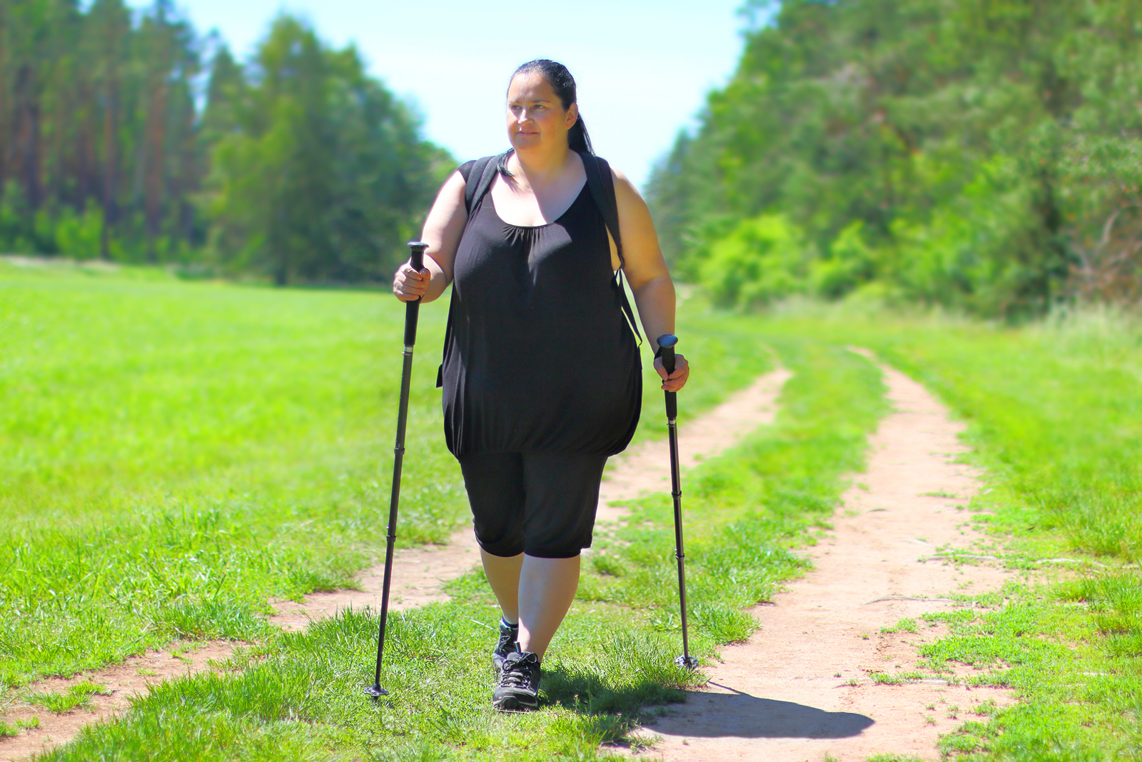 vrouw met obesitas wandelt in de natuur met wandelstokken.