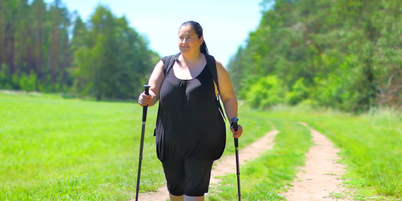 vrouw met obesitas wandelt in de natuur met wandelstokken.