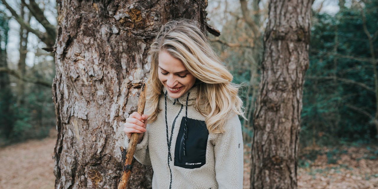 afbeelding van een vrouw in een fleecevest, buiten bij een boom.