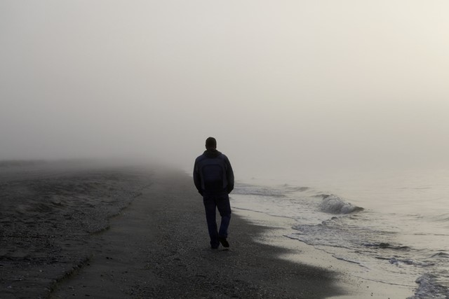 afbeelding van een man die wandelt in de mist aan zee.