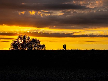 afbeelding van een wandelend stel tijdens een goudgele zonsondergang.
