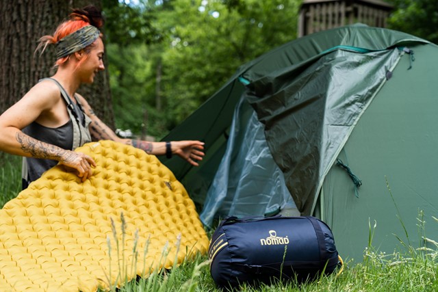 afbeelding van een vrouw met een slaapmatje, slaapzak en tent.