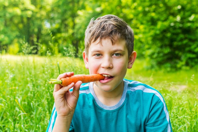 afbeelding van een jongen met een wortel in zijn mond.