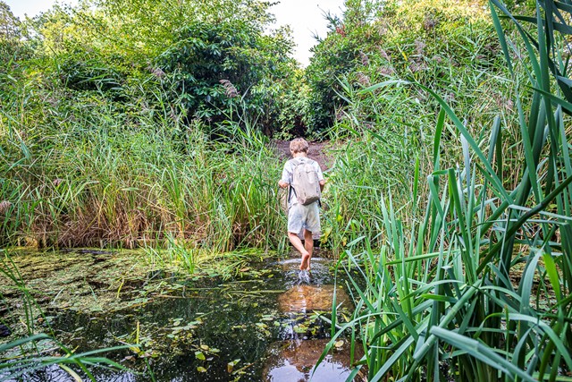 jongen loopt op stenen door het water op blote voeten.