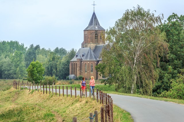 Duo wandelend op de dijk met een kerkje op de achtergrond