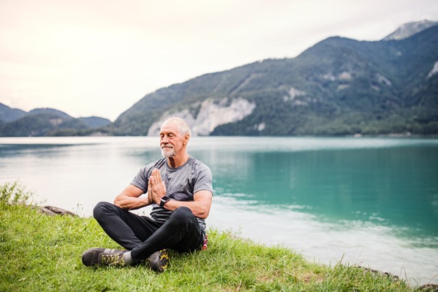 man mediteert aan een bergmeer op het gras.