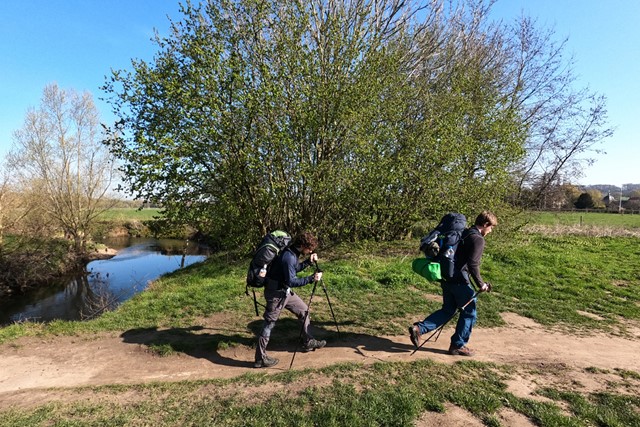 twee wandelaars met wandelstokken op een pad in het gras.