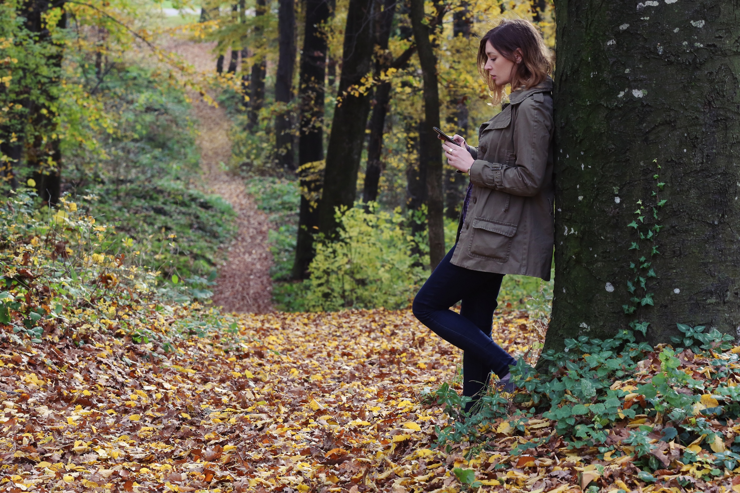 Vrouw op telefoon leunend tegen een boom