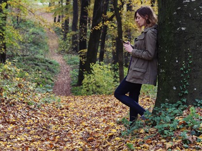 Vrouw op telefoon leunend tegen een boom