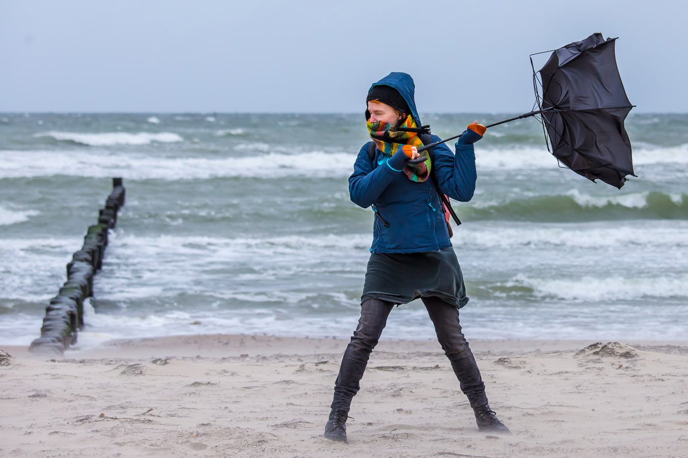 afbeelding van een wandelaar in de wind met een omgeklapte paraplu.