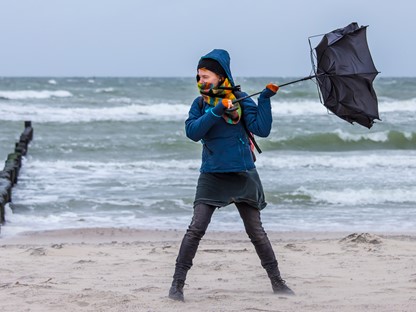 afbeelding van een wandelaar in de wind met een omgeklapte paraplu.