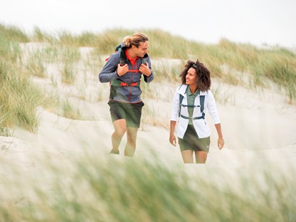 Twee personen wandelen in de duinen door het zand