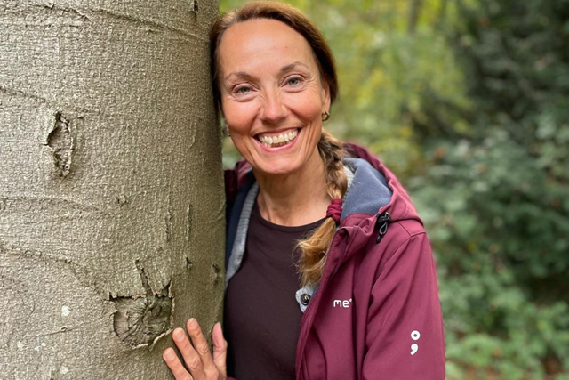 Wandeltrainer Linda Schuurs leunt tegen boom en kijkt lachend in de camera