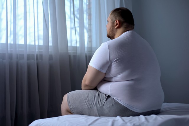 man zit in slaapkamer voor zich uit te staren.