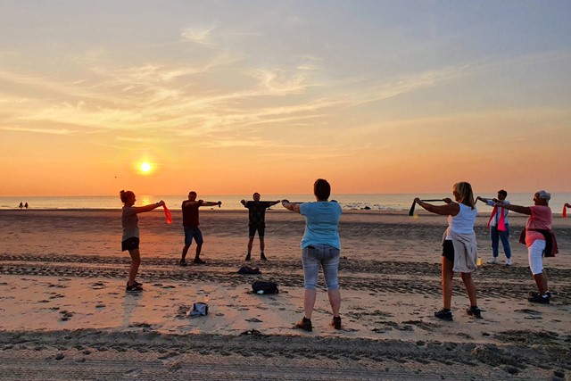 Wandelclub doet met een groep mensen een oefening op het strand bij ondergaande zon.