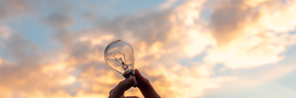 Gloeilamp in de hand van een persoon met lucht in de achtergrond