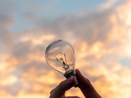 Gloeilamp in de hand van een persoon met lucht in de achtergrond