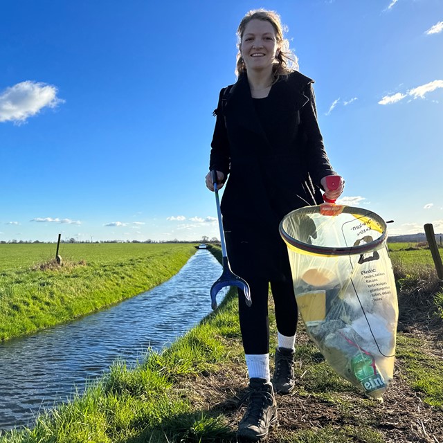 afbeelding van Annelies langs een sloot met een afvalzak en grijper.