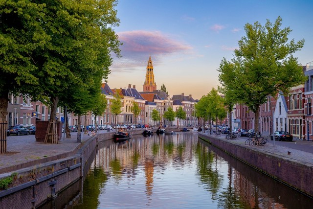 afbeelding van een gracht met bomen en een kerk.